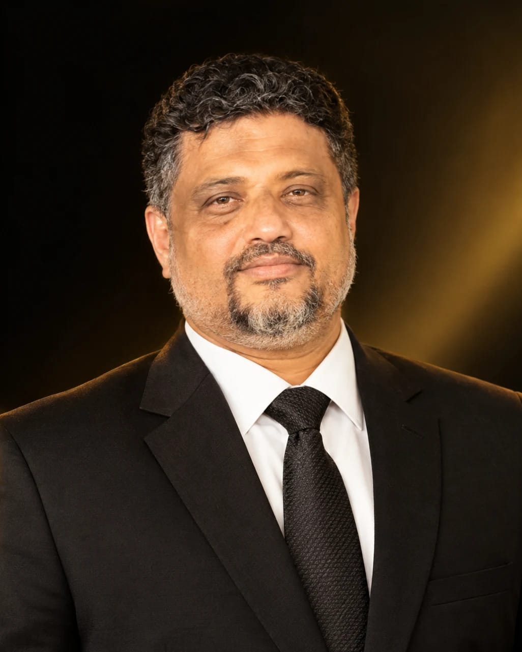 Portrait of NP Ashraf Haji, founder of Fragrance of France, in a dark suit against a black and gold backdrop